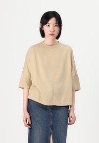 Beige short-sleeved top with a round neckline, featuring a loose fit. Paired with a dark denim skirt with a front slit and slight fraying.