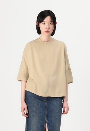 Beige t-skjorte med kort erme og rund hals, med en løs passform. Kombinert med en mørk denimskjørt med en slitt front og lett slitasje.