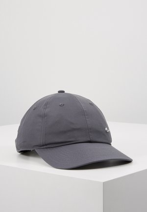 Mørkegrå Nike baseballkasket med lille sølv Swoosh-logo foran, hvilende på en hvid overflade mod en lys grå baggrund.