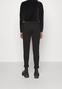 Černá sametová zkrácená mikina v kombinaci s černými slim-fit kalhotami. Oblečení se vyznačuje hladkou texturou a minimalistickým designem bez viditelných log.