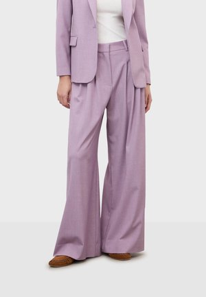 Femme portant un pantalon lavande taille haute à jambes larges et un blazer assorti sur un haut blanc, assortis à des mocassins en daim marron.