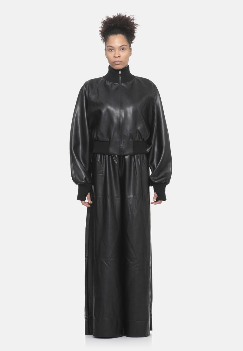 Giubbotto in pelle nera corto con maniche lunghe, polsini a coste e colletto alto, abbinato a una lunga gonna in pelle nera, di texture liscia.