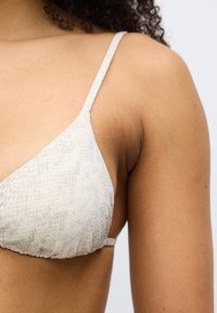 Τριγωνικό πάνω μέρος μπικίνι σε ανοιχτό γκρι χρώμα με διακριτικό μοτίβο φίδιου. Ρυθμιζόμενοι λεπτοί ιμάντες και ραμμένο ύφασμα στη βάση.