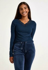 Navyblauw top met lange mouwen en een V-hals met kanten rand, gecombineerd met navyblauwe velours broek met verstelkoord.