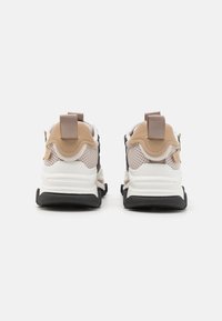 Sneaker chunky con tomaia in rete beige, suola in gomma bianca e dettagli neri; presenta linguette di apertura e dettagli texturizzati sul tallone.