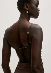 Bruine, mouwloze jurk met een geraffineerde textuur, met dunne bandjes en metalen hardware op de rug. Gladde stof met een aansluitende silhouet.