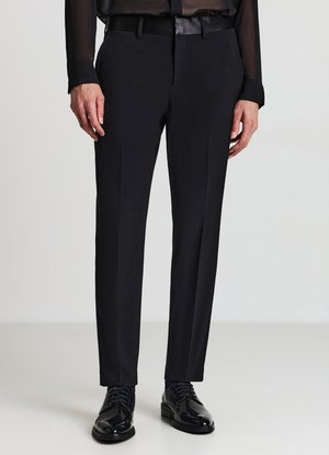 Schwarze, maßgeschneiderte Hose mit schmaler Passform, glatter Textur und Bügelfalte vorne. Kombiniert mit glänzenden schwarzen Lederschuhen.