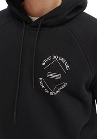 Sort hættetrøje lavet af blødt stof med et hvidt printet motiv, hvor der er tekst omkring en diamantform, samt snoredetaljer.