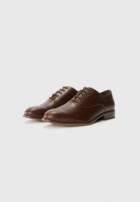 Brown leather Oxford shoes with a smooth texture, pointed toe, perforated detailing, and a low stacked heel. Laced closure detail.