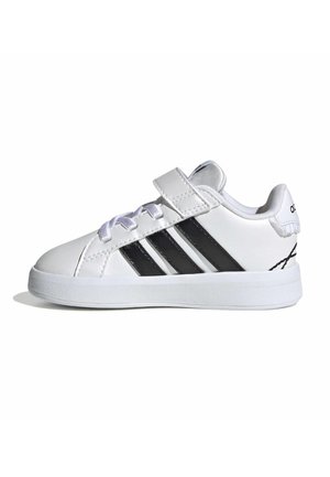 Sneaker bianca a taglio basso con strisce nere, lacci e cinturino in velcro, e suola spessa su sfondo bianco.