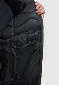 Pufferjack met een interieur in donkerblauw met een gewatteerde textuur, voorzien van een ritssluiting en meerdere zakken voor opbergruimte.