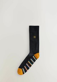 Calzino nero con parte superiore di un colore solido, punta gialla e motivo a strisce multicolori nella parte inferiore. Presenta un piccolo logo giallo.