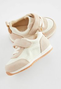 Beige und weiße Sneaker mit Wildlederakzenten, strukturiertem Canvas, Klettverschluss und Gummisohle; verfügt über gestickte Details und eine Zuglasche.
