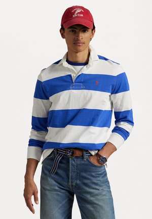 Blå og hvid stribet langærmet polo-shirt med krave, med et lille logo, parret med lyseblå jeans og et brunt bælte. Rød kasket.
