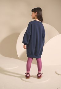 Felpa oversize blu navy, leggings viola con sfumatura e scarpe marroni con dettagli rosa. Tessuto liscio e vestibilità comoda.
