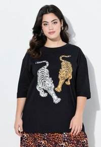 Camiseta negra de gran tamaño con estampados de tigre en blanco y naranja. Presenta un cuello redondo y mangas de 3/4. Combinada con una falda de estampado de leopardo.