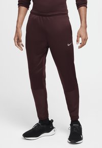 Burgundowe spodnie sportowe o zwężanym kroju, wykonane z teksturowanej tkaniny, z elastycznym pasem i kieszeniami po bokach. Zawierają mały akcent w postaci logo.