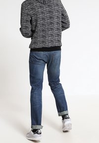 Svart och vit strukturerad hoodie, blå denimjeans med uppvikta ben och vita sneakers med svarta detaljer. Sedd bakifrån.