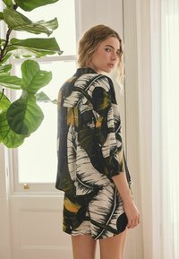 Blusa de manga corta con patrón de hojas en blanco y negro, combinada con pantalones cortos a juego, con acentos audaces en verde y amarillo y un ajuste relajado.