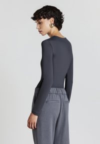Body aderente grigio a maniche lunghe con una texture liscia, abbinato a pantaloni grigi a vita alta con un cinturino arricciato e tasche.
