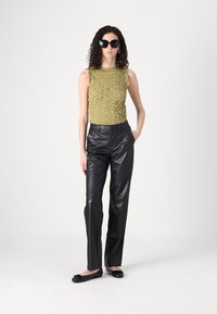 Olive-texturerad ärmlös topp, svarta läderbyxor, svarta lägenheter och oversized solglasögon. Enkel design, släta material, figurnära silhuett.
