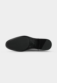 Semelle de chaussure habillée en cuir noir avec des zones de grip texturées au talon et à la boule, indiquant la taille 42 et l'empreinte de la marque sur la partie lisse.