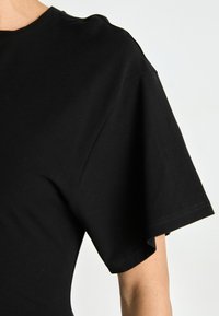 Sort t-shirt med korte ærmer og en afslappet pasform. Fremstillet af blødt stof med en let glans, der fremhæver en ren udskæring og syninger.