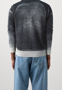 Grauer und schwarzer Gradient-Pullover mit geripptem Saum und Bündchen. Die Rückansicht zeigt eine weiche Textur und eine lockere Passform, kombiniert mit hellblauen Jeans.