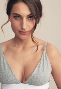 Grå bomullsbustier med V-ringad design, tunna justerbara band och en vit rem nertill. Mjuk textur med minimalistisk stil.