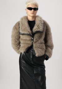 Nepbont cropped jack in lichtbeige met een brede kraag en zwarte leren accenten. Gecombineerd met een strakke zwarte leren rok.