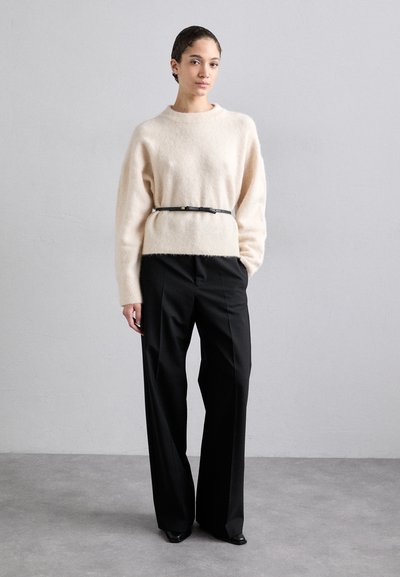 Beige, fluffy genser med rund hals, svart lærbelte i midjen, og høyt midjede svarte bukser med brede ben og glatt tekstur.