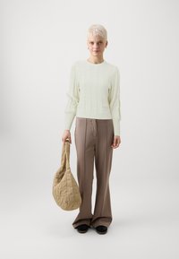 Strikket lys grønn genser med et teksturert mønster, beige quiltet veske, taupe vide bukser og svarte slip-on sko.