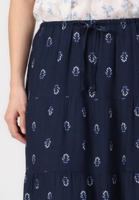 Fustă maxi din bumbac, de culoare bleumarin, cu un model floral alb. Prezintă un talie elastică cu un șnur, un design în straturi și o textură netedă.