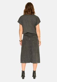 T-shirt gris à manches cape associée à une jupe en denim gris mi-longue. La jupe comporte deux poches arrière et des coutures visibles. Bottines noires.