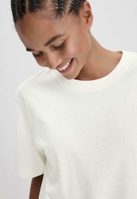 Lichtbeige T-shirt met korte mouwen en een ronde hals, gemaakt van zachte katoenstof. Minimalistisch ontwerp zonder zichtbare patronen of accenten.