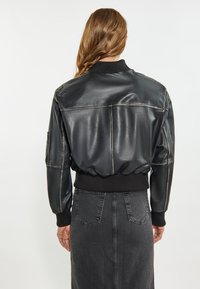 Giacca bomber in pelle nera con polsini e vita a coste, caratterizzata da una texture liscia e dettagli di cucitura minimi. Vista posteriore mostrata.