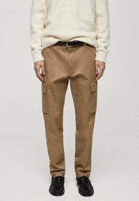 Beige cargo kalhoty s dvěma bočními kapsami, vyrobené z bavlny, s rovnou siluetou a volným střihem. Nosené s bílým pleteným svetrem.