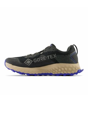 Sort og grå Gore-Tex terrænløbesko med beige bikagemønster i sålen og lilla slidbane, set fra siden, snøret med sorte og hvide snørebånd.