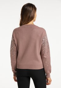 Pulover tricotat roz cu mâneci lungi, decorat cu paiete argentii pe umeri. Bază și manșete cu dungi, croială lejeră. Textură moale.