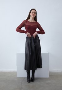 Bordó hosszú ujjú áttetsző blúz, amelyet egy redős fekete bőr szoknyával párosítanak, kiegészítve térd fölé érő fekete csizmával. Egyszerű, modern design.
