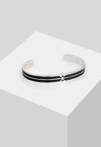 Bracciale rigido in argento con due strisce di smalto nero. Ha una superficie liscia e lucida, caratterizzata da un design minimalista e estremità aperte.