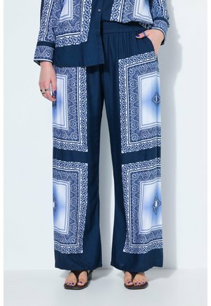 Marineblauwe wijde broek met witte en blauwe ingewikkelde vierkante patronen, elastische tailleband, gecombineerd met een bijpassend patroon overhemd en zwarte sandalen.