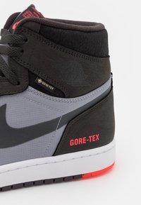 Gros plan sur une basket Air Jordan noire et grise avec une étiquette Gore-Tex et un texte rouge "GORE-TEX" sur le talon, avec une semelle blanche et des accents rouges.