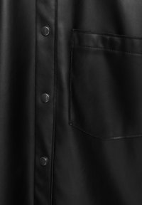 Chemise en cuir noir avec fermeture à boutons sur le devant, boutons-pression, texture lisse et une poche unique sur le côté gauche.