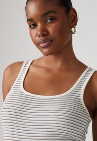 Top senza maniche a coste di colore crema con sottili righe orizzontali di tonalità diverse. Presenta un collo rotondo e una texture morbida.