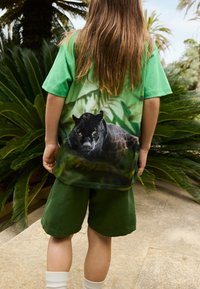 Zeleni pamučni majica s gradijentnim džungla dizajnom i grafikom crnog tigra na leđima. Uparen s zelenim šortsem i bijelim čarapama.