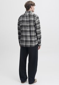 Svart og grå rutete flanellskjorte med knappet krage og lange ermer, kombinert med løse svarte bukser og brune sko.