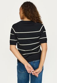 Črna pletena bluza s kratkimi rokavi, z belimi vodoravnimi črtami in rebrastim robom, nošena z modrimi jeans hlačami.