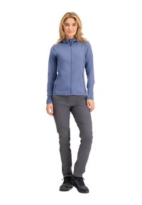 Lichtblauwe zip-up jas met capuchon, gecombineerd met grijze broek. De stof lijkt glad met ritszakken, en zwarte schoenen maken de outfit compleet.