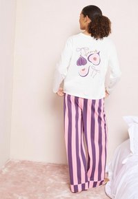 Hosszú ujjú, fehér pamut felső, hátul lila füge grafikával. Csíkos pizsamanadrág rózsaszín és lila színben, laza illeszkedésű kialakítással.